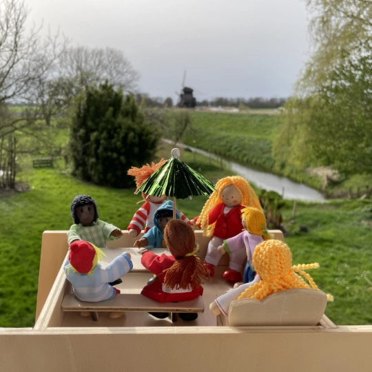 Een poppenfamilie geniet van de buitenlucht op het dakterras van hun poppenhuis.